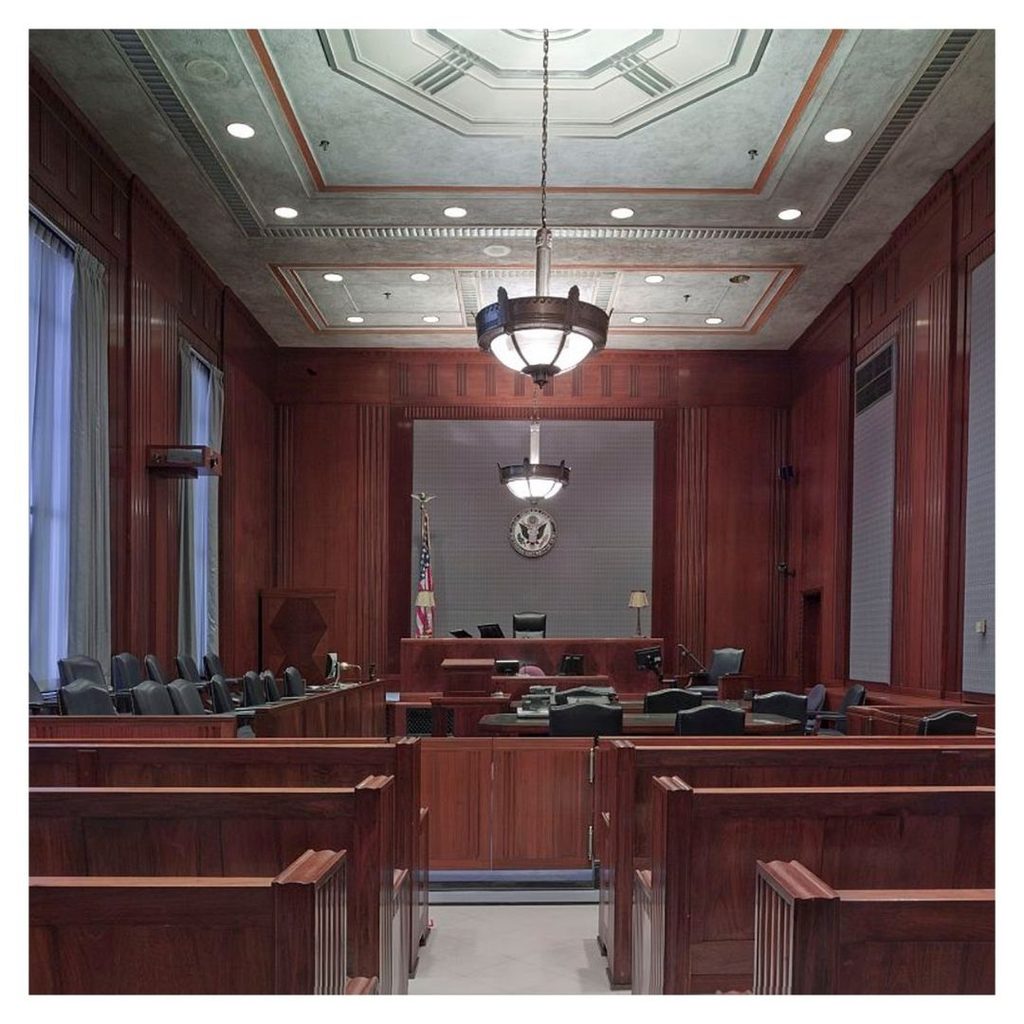 The interior of a courtroom. Photo is taken from the back of the room, so you can see the layout of the front of the room.