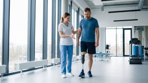 A physical therapist assists an amputee patient practicing walking with a prosthetic leg in a bright rehabilitation facility.