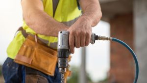 A close-up of a construction worker's hand gripping a large pneumatic drill on a job site.