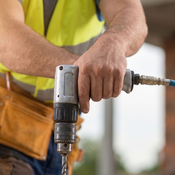 A close-up of a construction worker's hand gripping a large pneumatic drill on a job site.